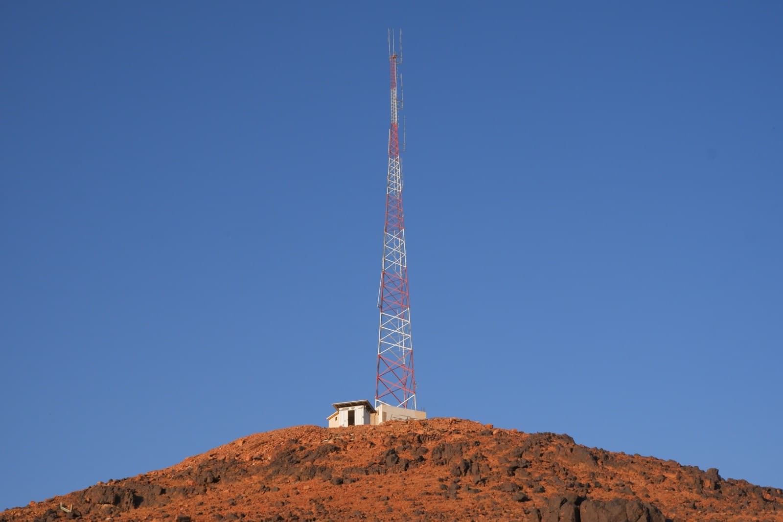A lattice radio mast on a rocky hilltop under a clear sky